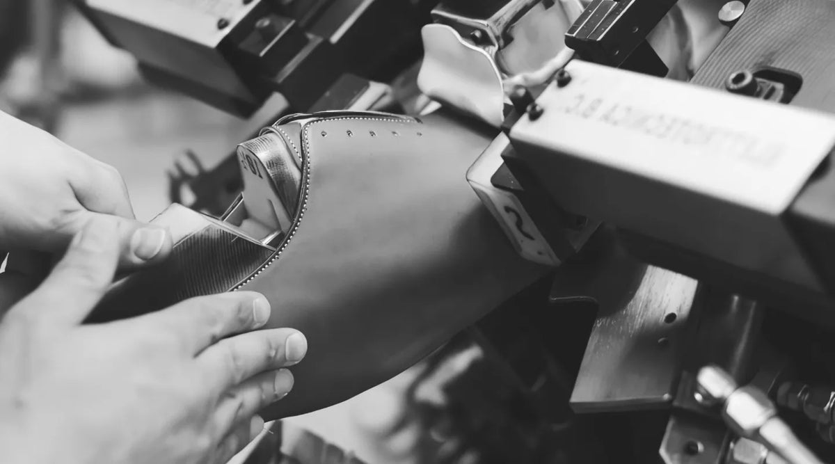 Shoemaker handcrafting a leather dress shoe with a machine in a workshop